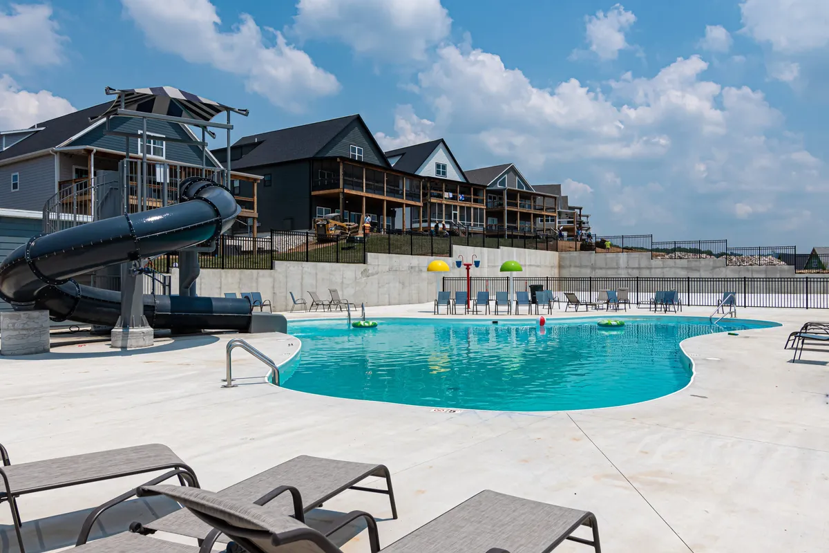 A vibrant outdoor swimming pool scene featuring a water slide, colorful umbrellas, and lounge chairs. The area is filled with the energy of swimmers and sunbathers, highlighting the fun and social atmosphere of the amenity.