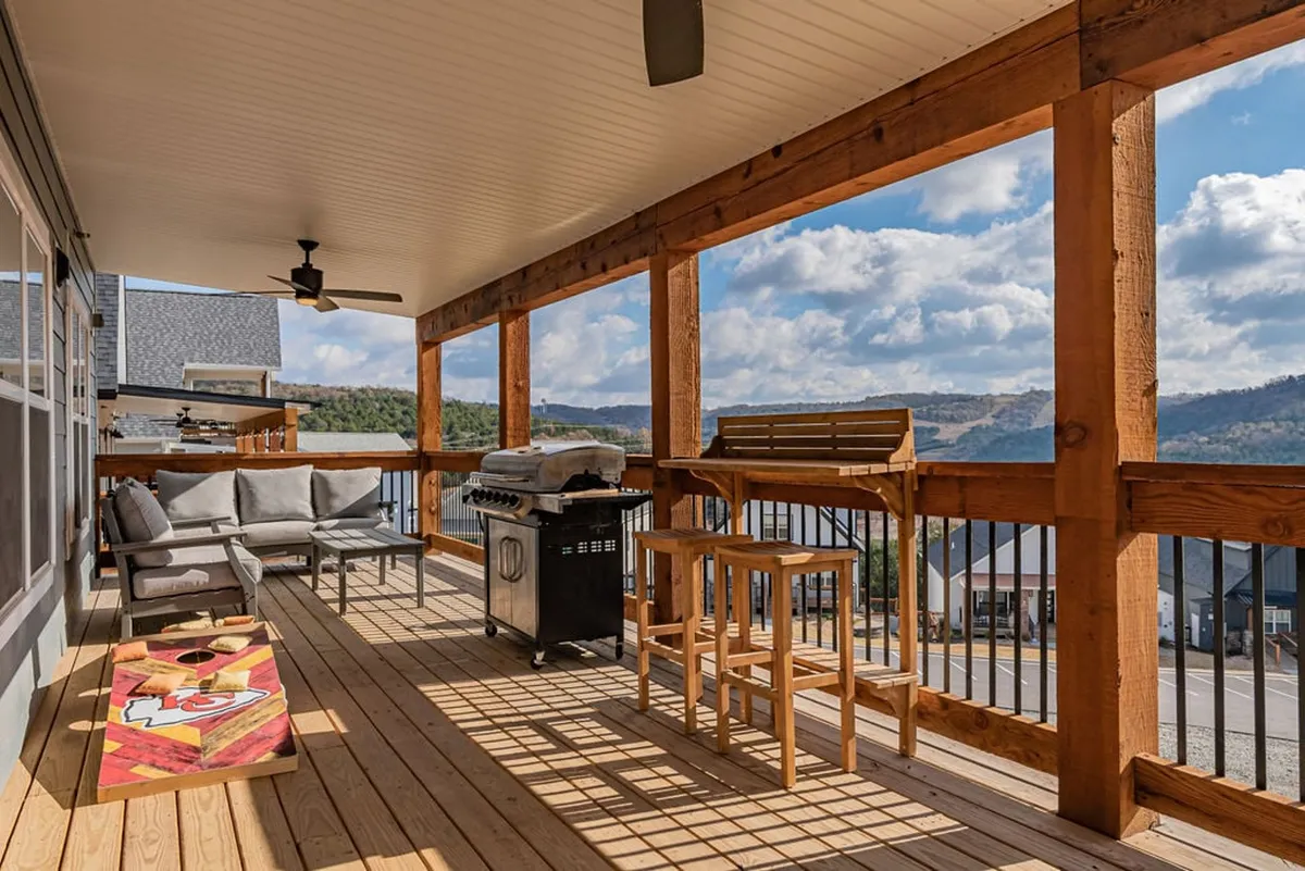 A relaxed outdoor seating area with a grill, bar stools, and a decorative cornhole board set up overlooking a scenic landscape. The area is ideal for barbecuing, outdoor dining, and playing games with friends or family, embodying the social and playful aspects of the retreat.