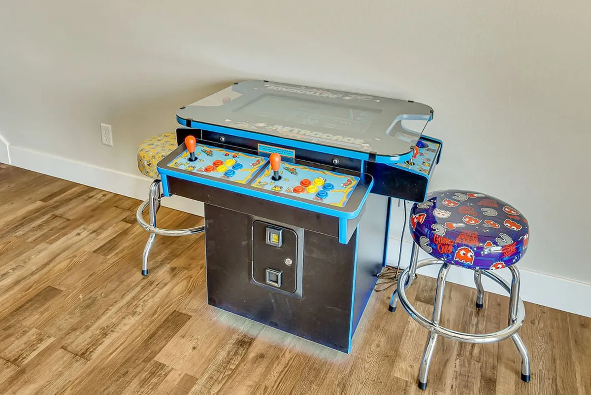 An arcade corner with a classic arcade game machine and colorful stools, designed for playful nostalgia and friendly challenges.