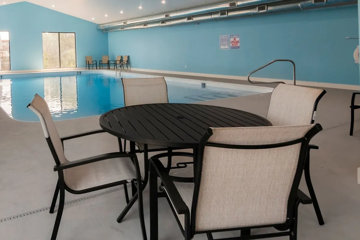 This image showcases the bright, indoor swimming pool area, featuring large windows that let in natural light, a calm pool, and seating areas for relaxation. The tranquil indoor setting promises leisure and fitness opportunities regardless of the weather.