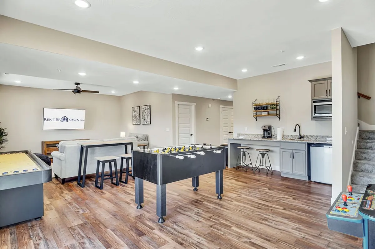 A vibrant game and lounge area featuring a foosball table, shuffleboard table, and comfortable seating adjacent to a kitchenette. The space is designed for friendly competition and easy socializing, with ample room for games and snacks.