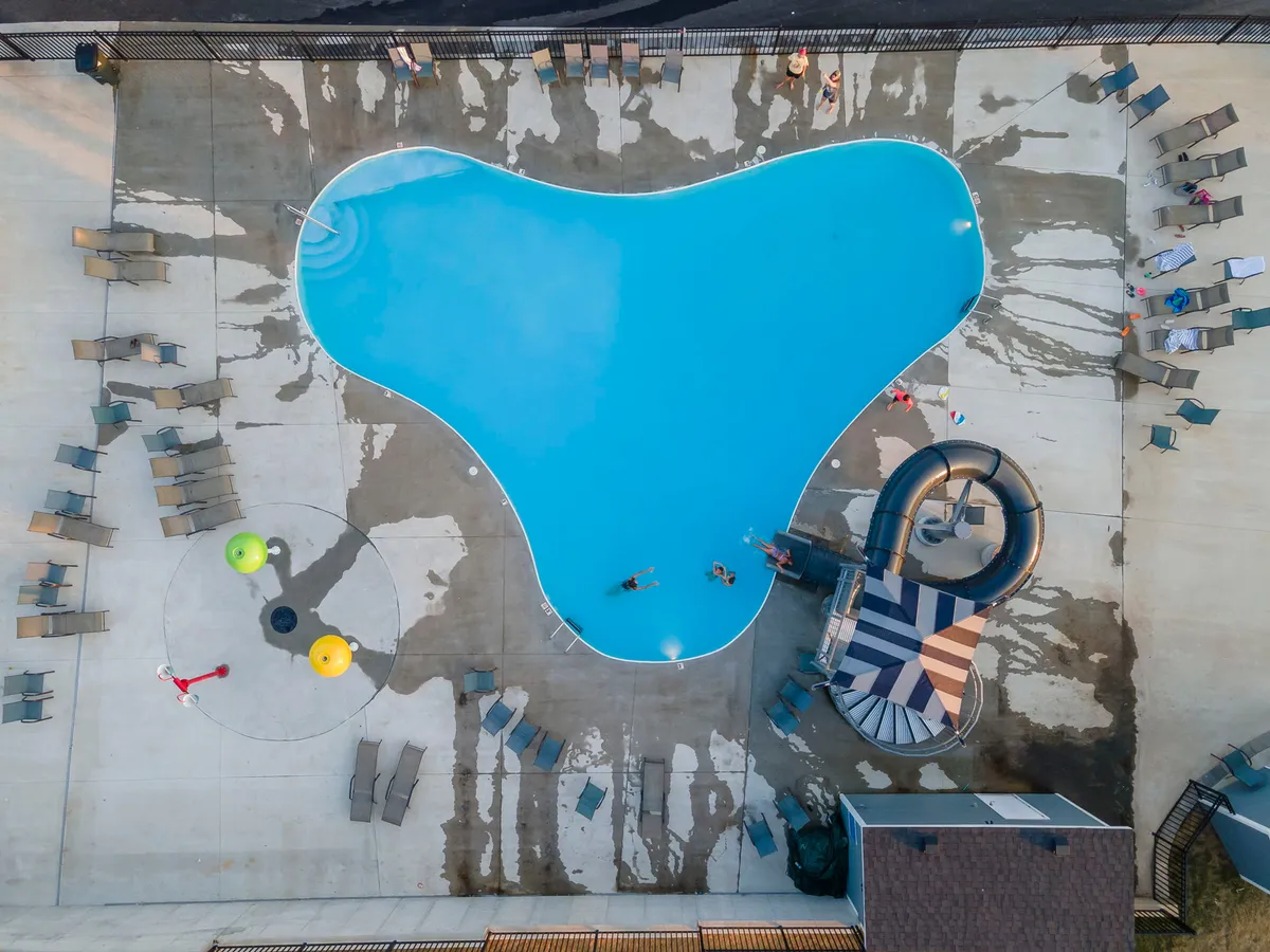 This exterior image captures a vibrant outdoor pool area complete with a water slide, colorful playground equipment, and inviting lounge chairs. The scene is lively, showing spaces perfect for swimming, sunbathing, and play, all in a well-maintained communal setting.