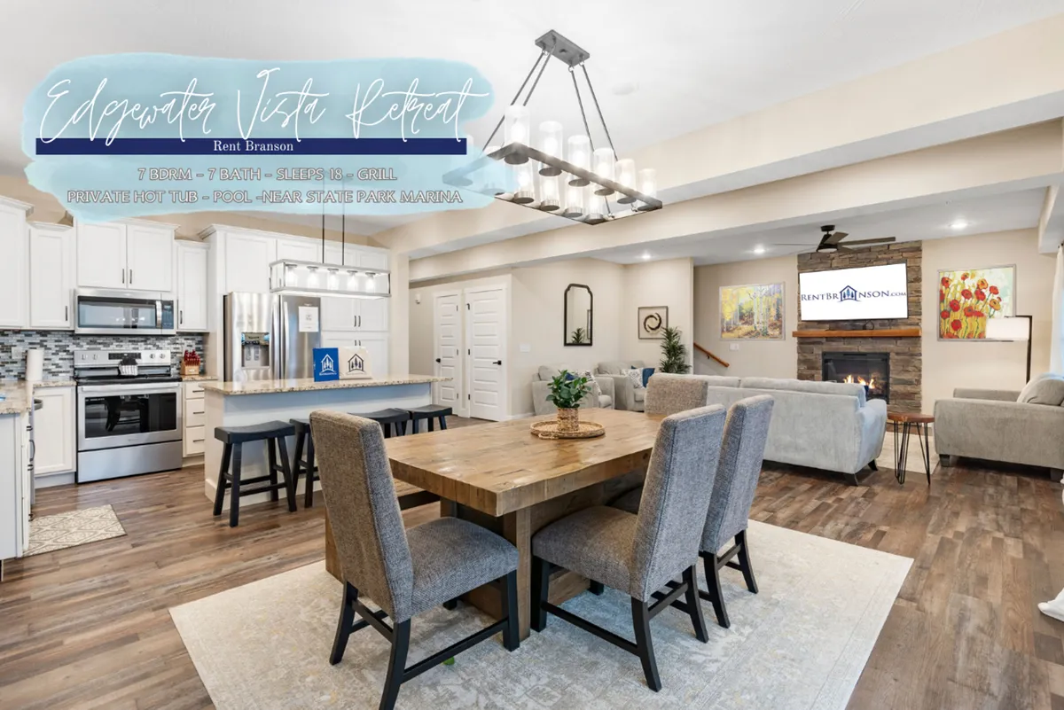 A spacious, open-concept living area featuring a large dining table, a kitchen island, a cozy fireplace, and a comfortable sofa area all illuminated by a warm chandelier. Expansive windows allow natural light to fill the room, creating an inviting atmosphere perfect for gatherings.