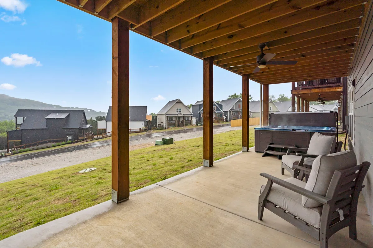 An exterior shot of a covered patio featuring a hot tub, comfortable seating, and partial views of the surrounding neighborhood and mountains in the background. The space appears secluded, tranquil, and ideal for relaxation, with a peaceful atmosphere enhanced by scenic views.