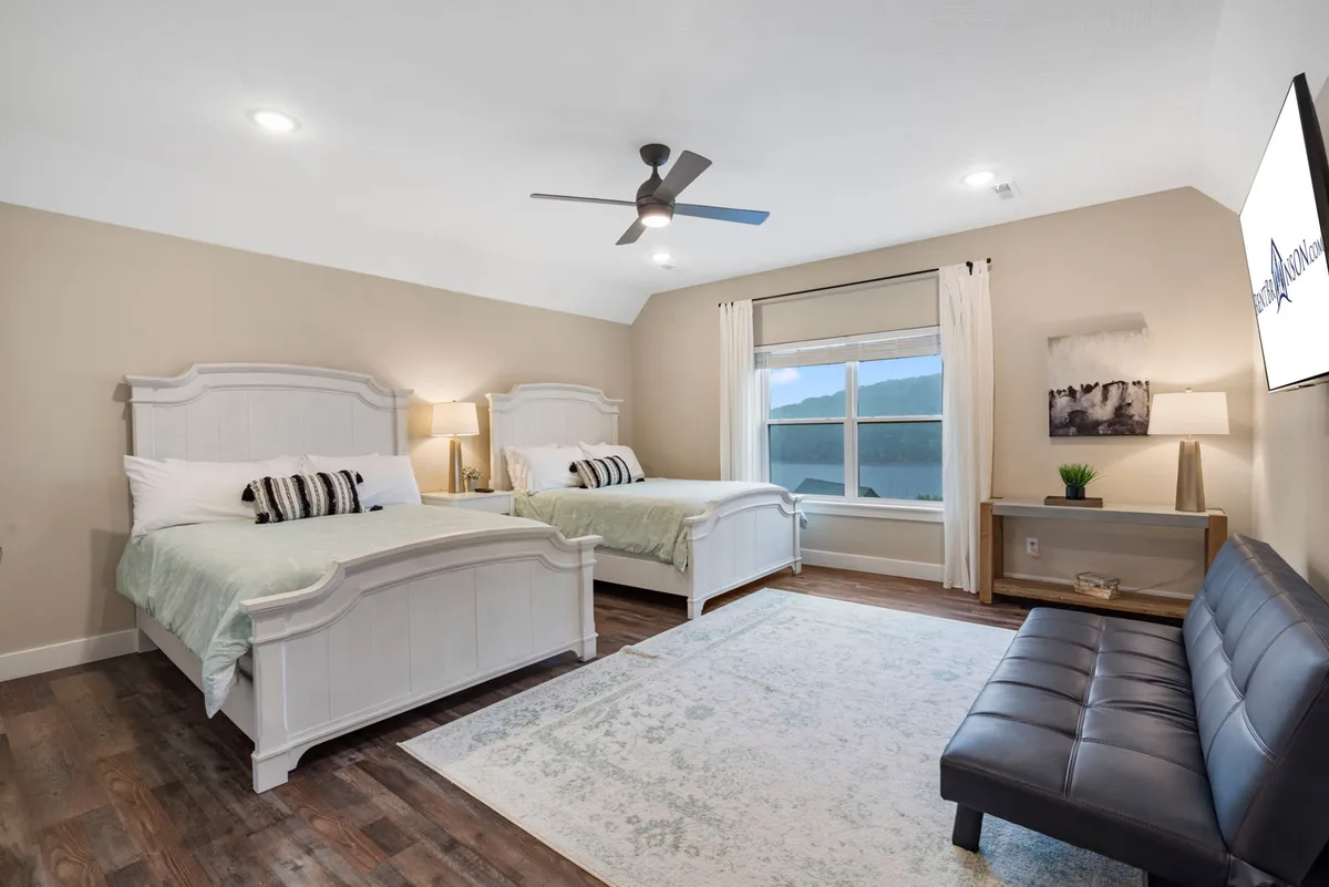 A cozy and serene double-queen room featuring two beds facing a large window that fills the space with natural light. There is also a sofa and stylish light fixtures, offering a welcoming, spacious environment suitable for families or groups. The room's calm color palette and careful arrangement highlight both comfort and the opportunity for relaxation with a view.
