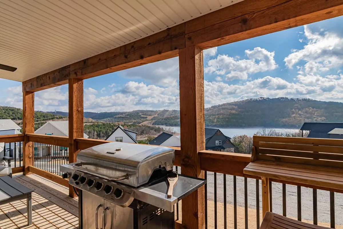 This image captures an outdoor seating area with a grill, wooden railing, and a panoramic view of Table Rock Lake in the background. The serene setting invites guests to relax, barbecue, or simply take in the beautiful lakefront scenery.