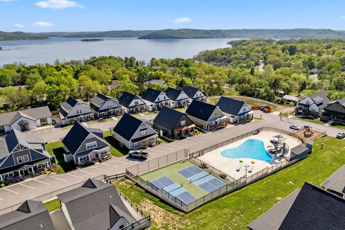 This exterior shot captures a sweeping view of the resort’s swimming pool, adjacent pickleball courts, the shimmering lake in the background, and surrounding homes. The pool area includes lounge chairs for sunbathing and the communal recreational space is lively and inviting.