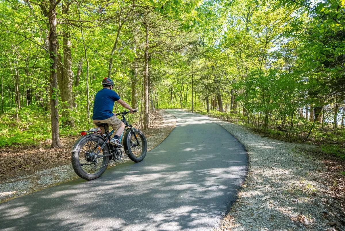 A winding walking path weaves through lush greenery, with a bicyclist traveling along the route. The path emanates a sense of adventure and connects guests to the surrounding natural landscape, ideal for walking or biking excursions.