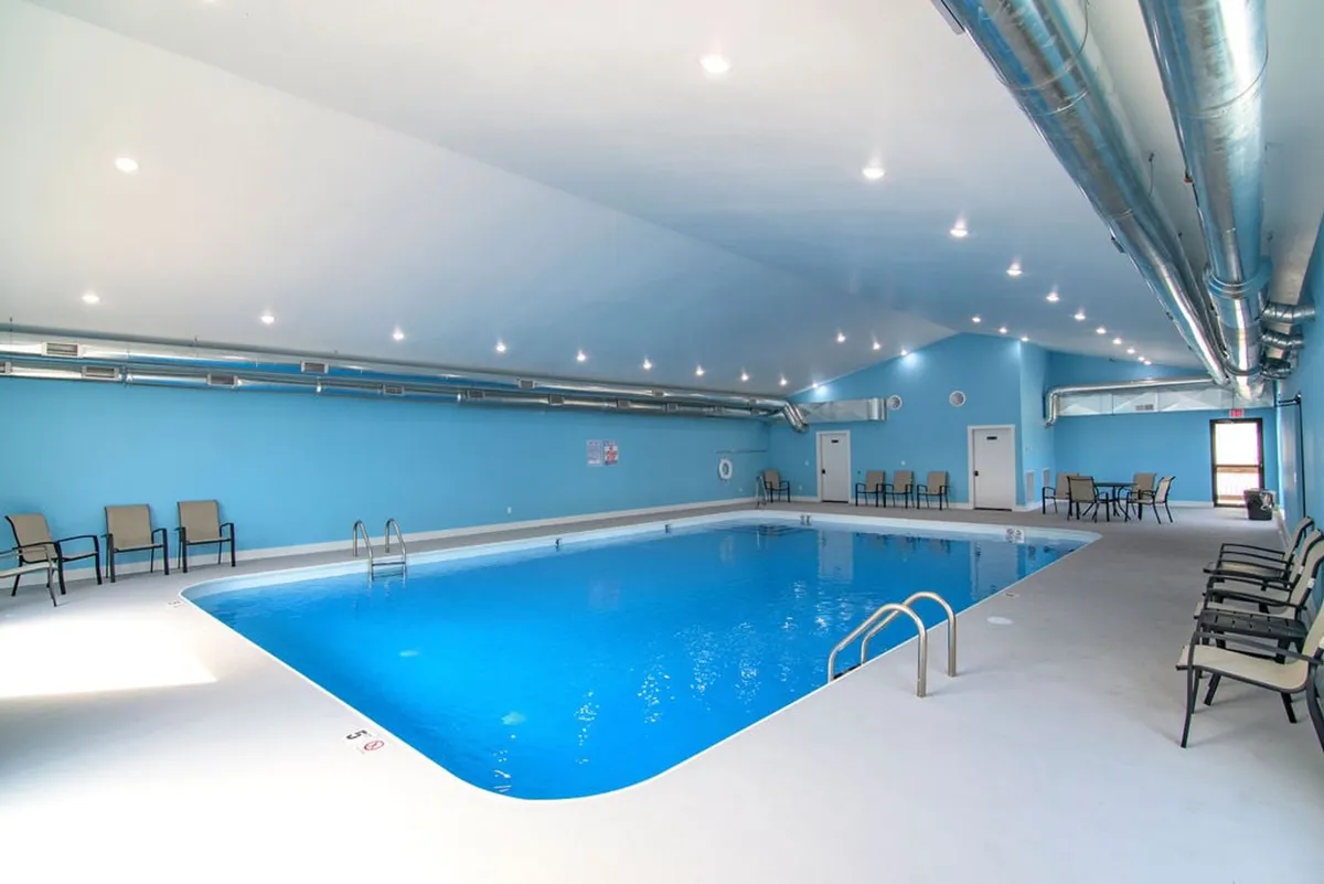 A bright, calm interior features the resort’s indoor swimming pool, flanked by blue walls and a comfortable seating area. The inviting water and tranquil atmosphere highlight a relaxing, all-weather amenity for guests.