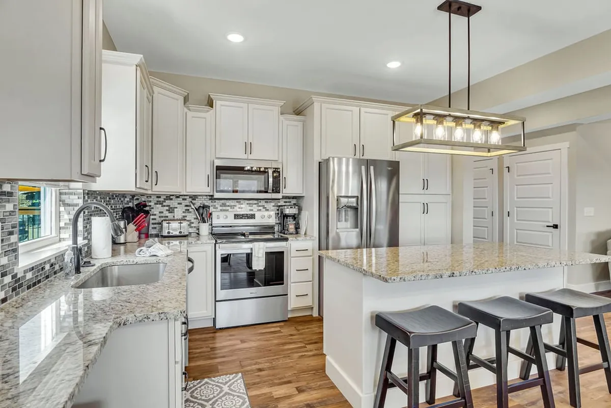 A stylish kitchen with granite countertops, island seating, stainless steel appliances, and a tiled backsplash. The space is designed for both cooking and socializing, with ample counter space for preparing meals and sharing snacks.